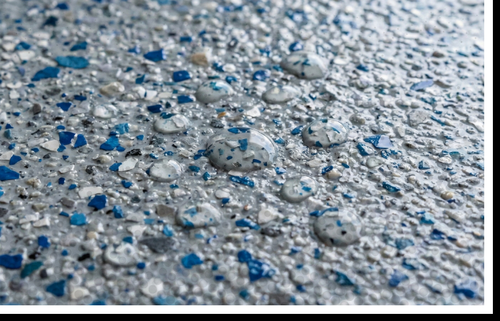 Close-up macro shot of a textured, slip-resistant polyurea floor coating with blue and grey flakes and water droplets.