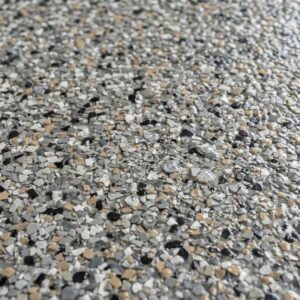 A close-up view of a textured concrete overlay coating with anti-slip chips and water droplets, demonstrating its safety features.