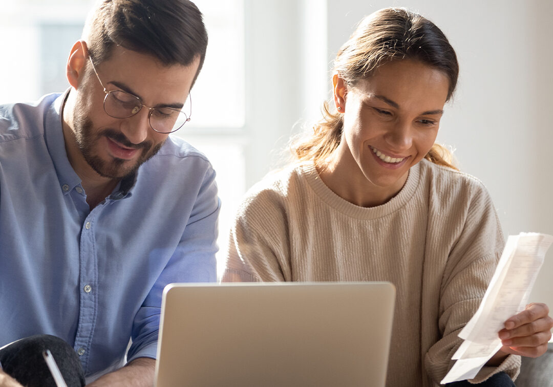 a man and woman smiling while looking at a bill